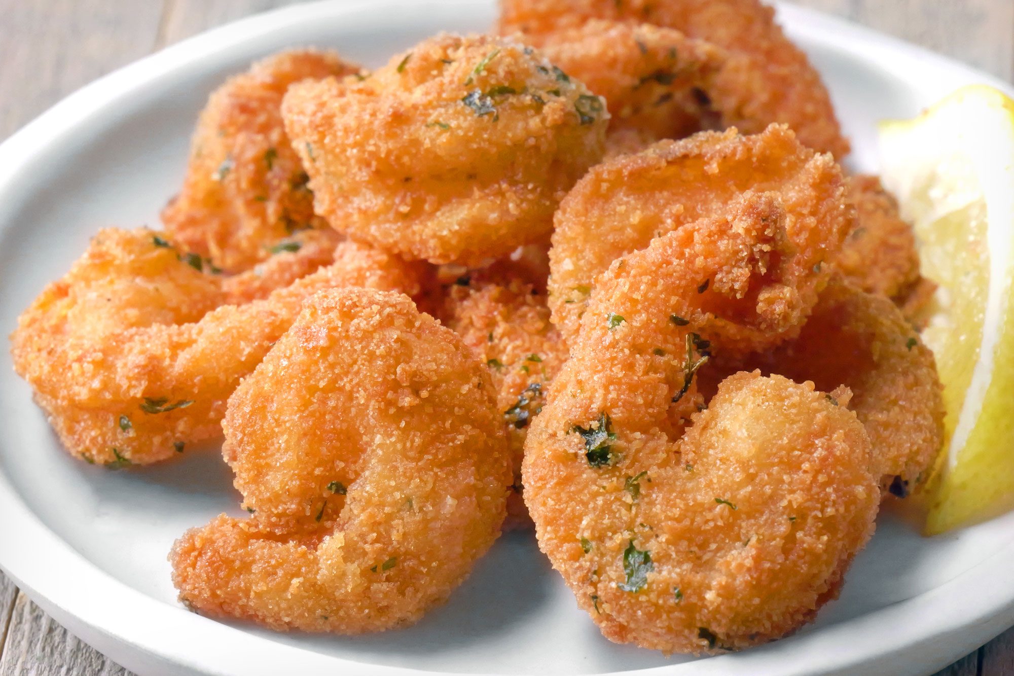 Close shot of Popcorn Shrimp; served on plate with sauce and lime wedges; wooden background;