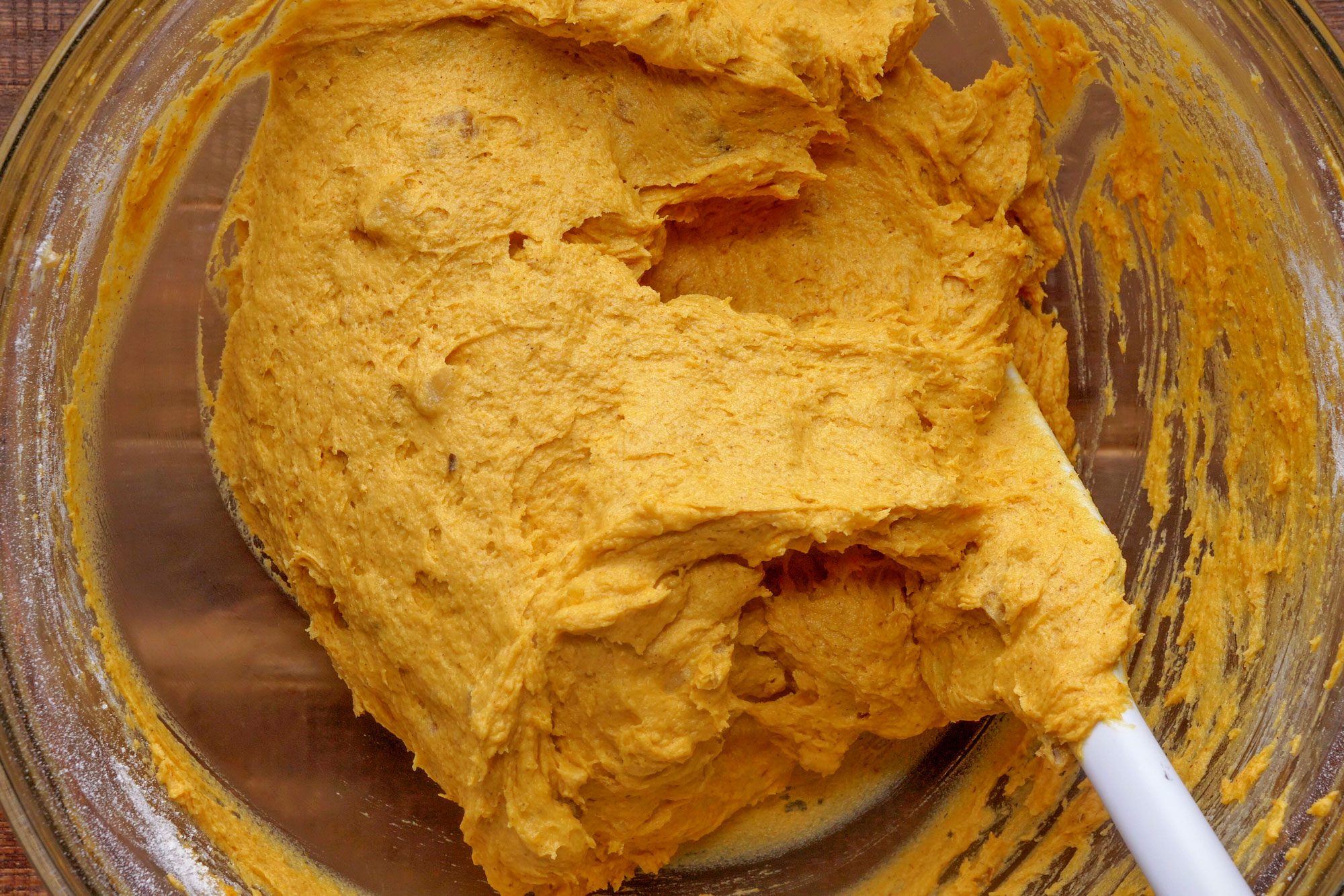 overhead shot of pumpkin cookie batter with spatula in a glass bowl