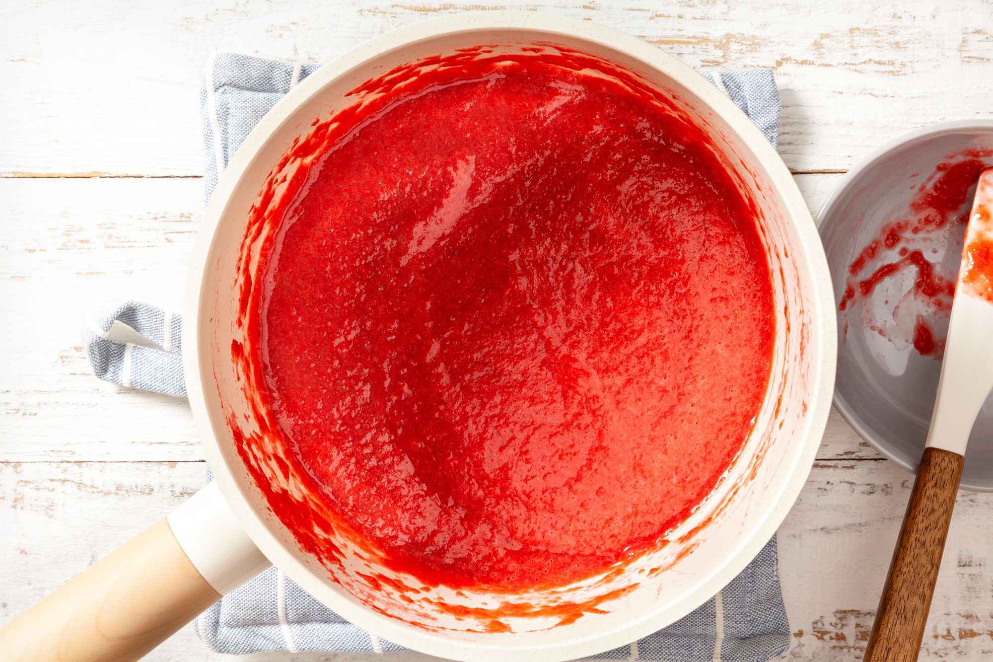 overhead shot of strawberry puree in large saucepan on white wooden background
