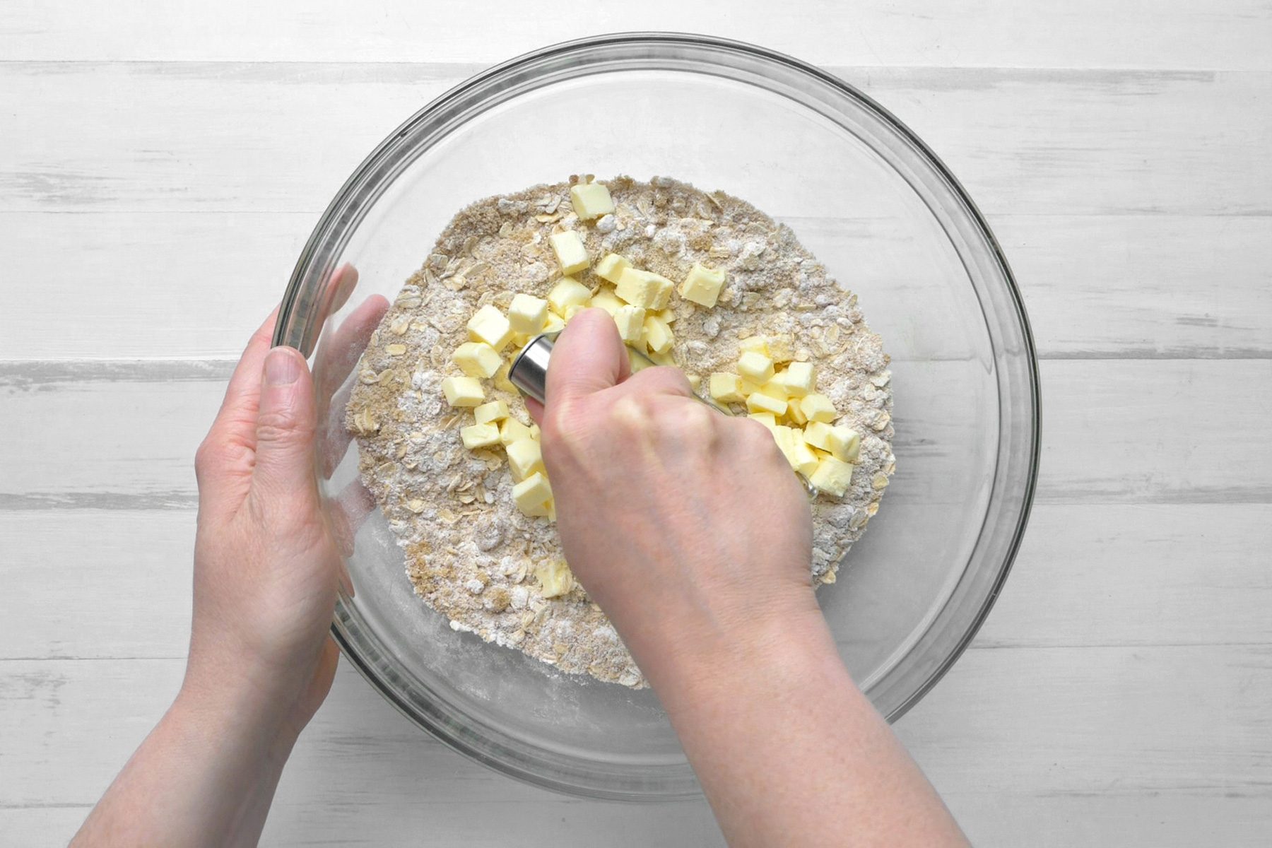 A hand mixing the flour, oats, brown sugar and cinnamon in a glass bowl