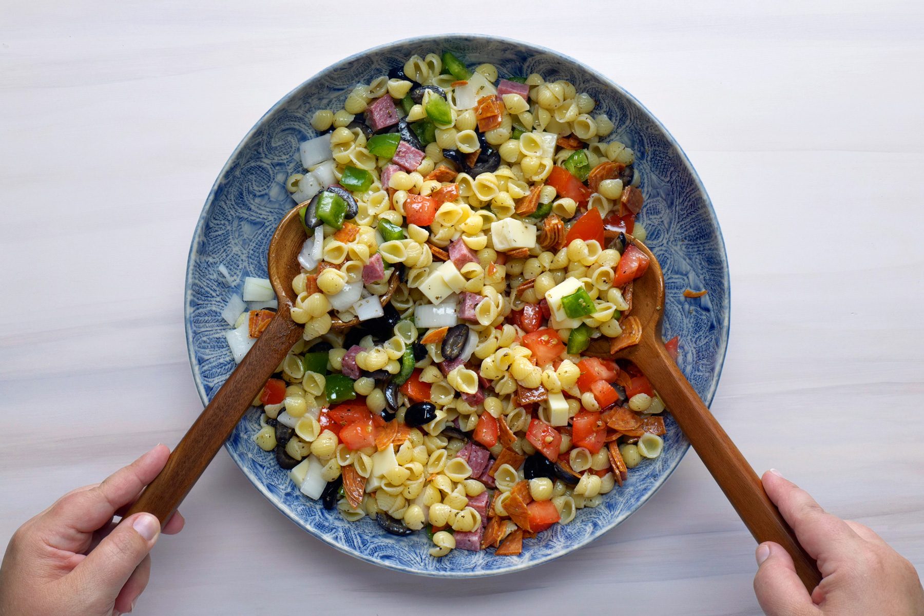 Mixing the ingredients for the Italian pasta salad together with wooden spatulas 