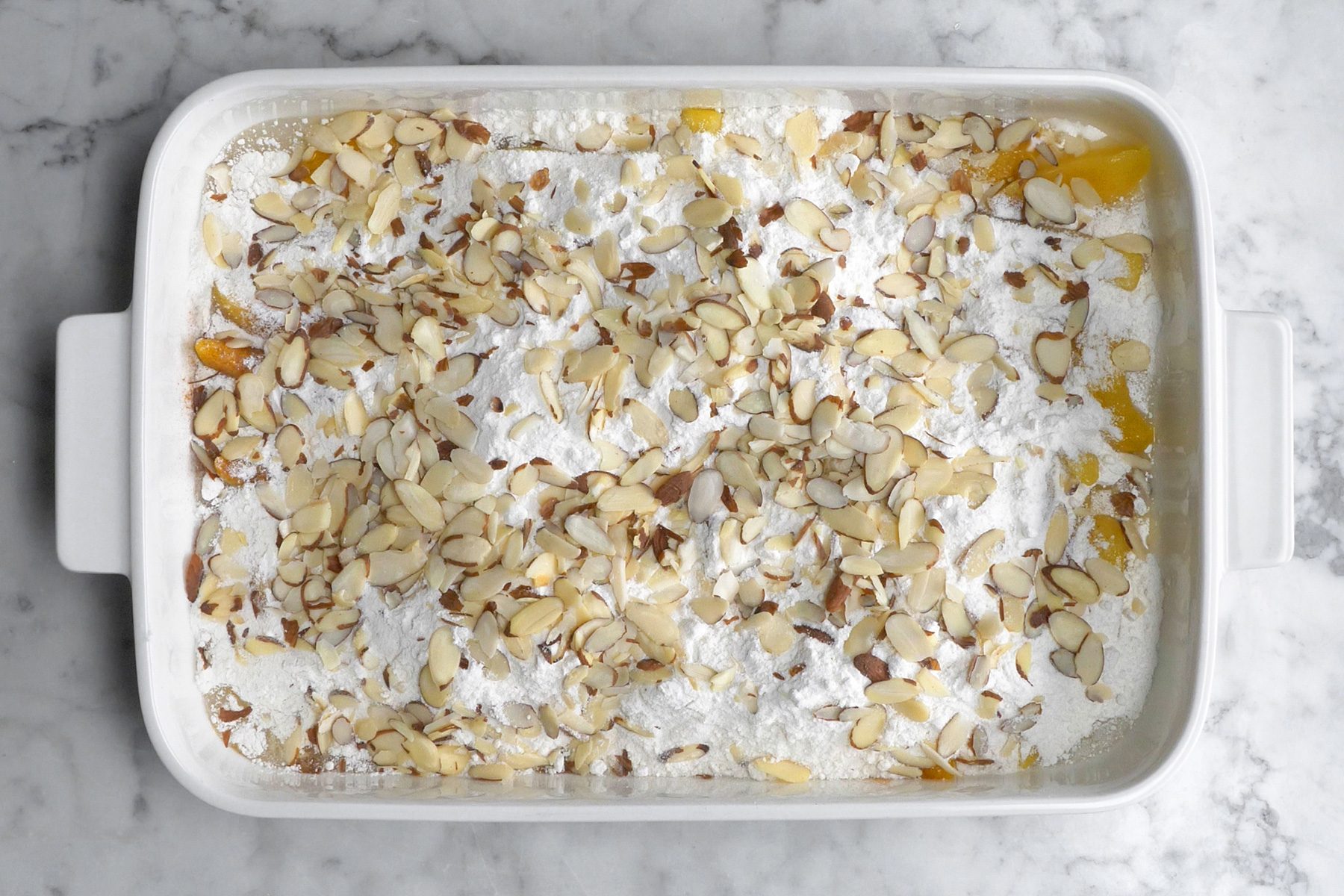 A white baking dish layered with cake mix, almonds, and other ingredients