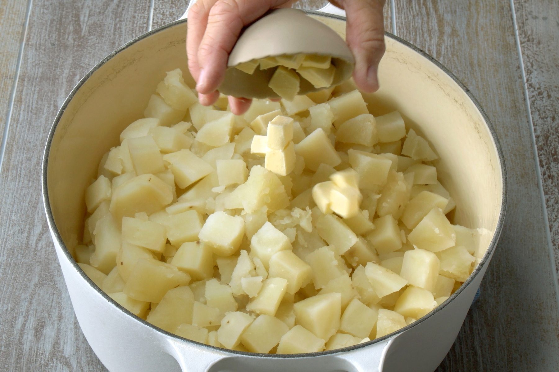 Butter being put into the bowl of boiled potatoes