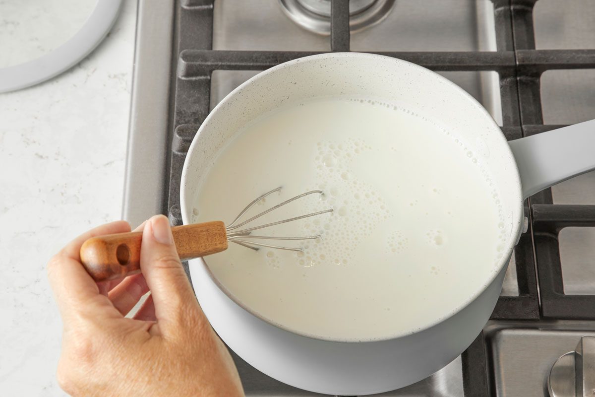 overhead view of a hand stirring milk in a saucepan to make evaporated milk