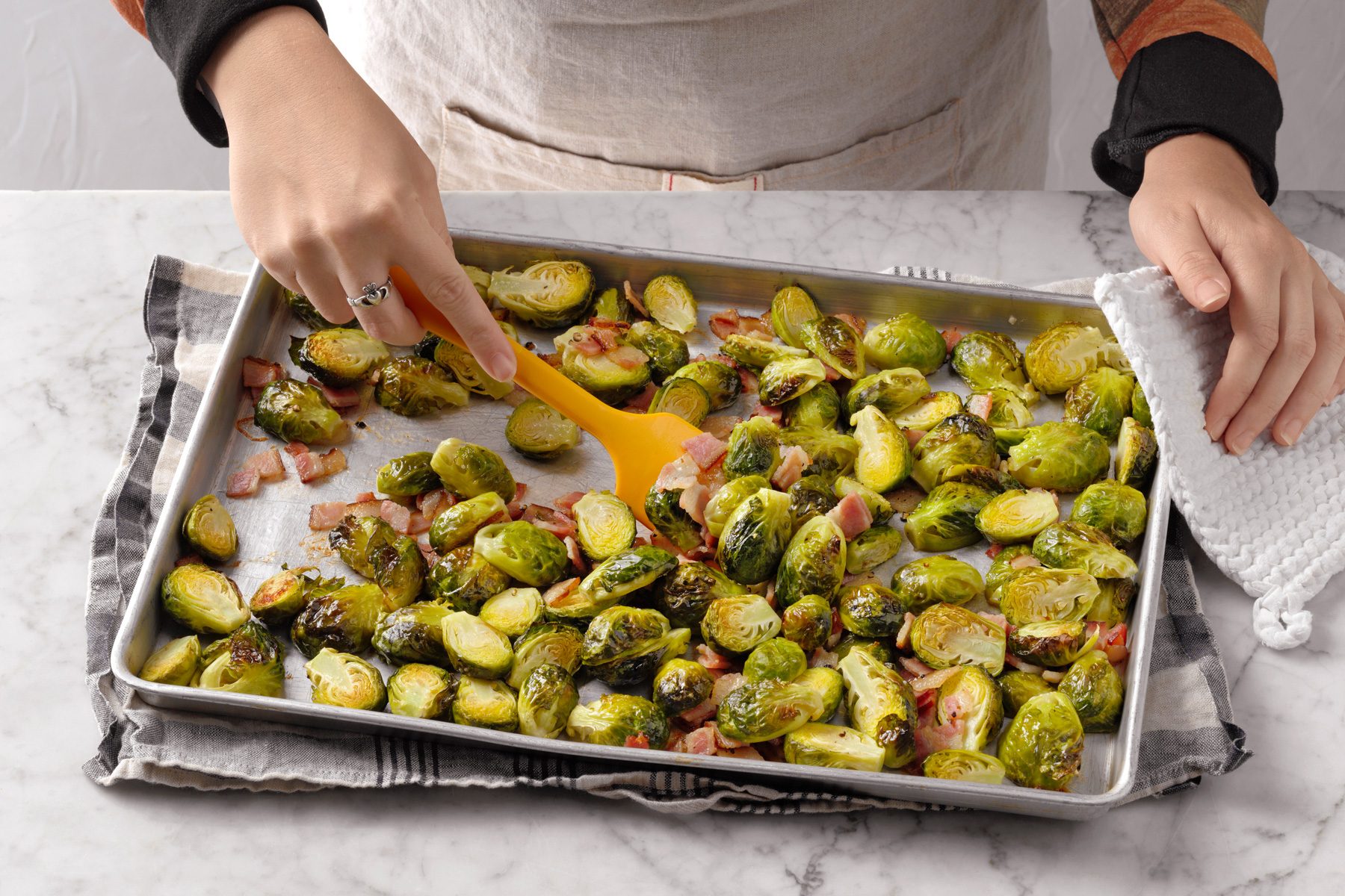 A person mixing and Brussels Sprouts with Bacon in a baking tray.