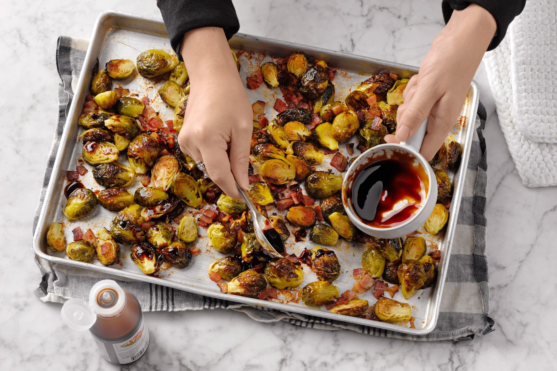 A person adding sauce in Brussels Sprouts with Bacon in a baking tray.