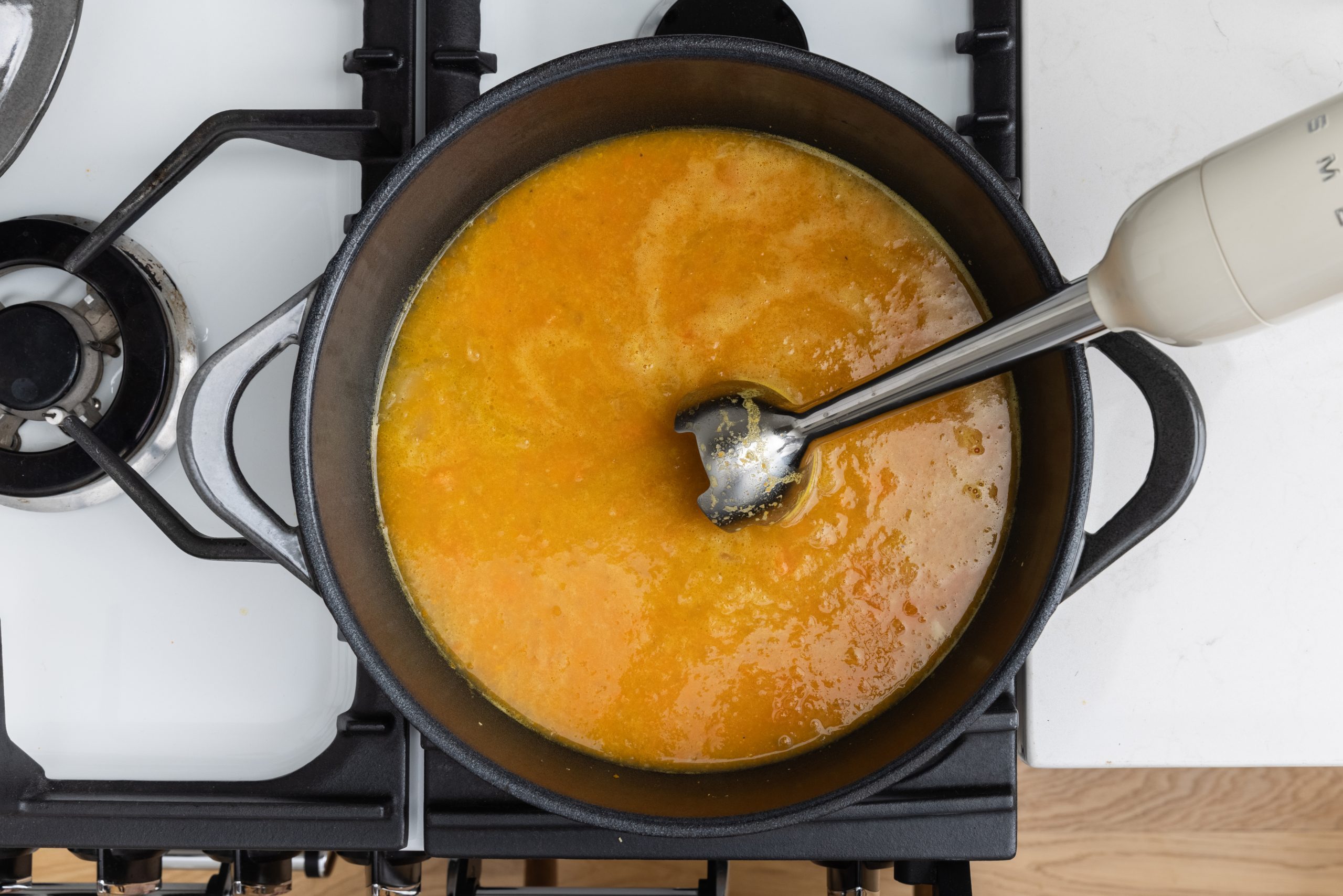 Soup in dutch oven on stove top being blended.