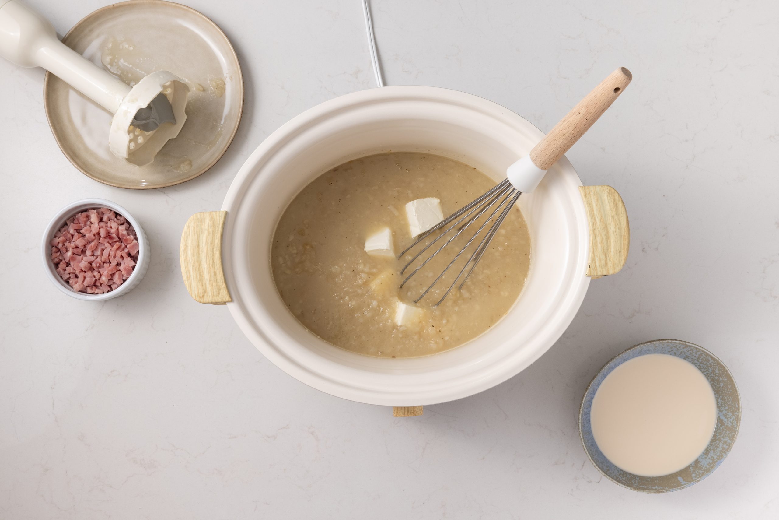 Potato and Ham Soup being finished with cream cheese, ham and milk.