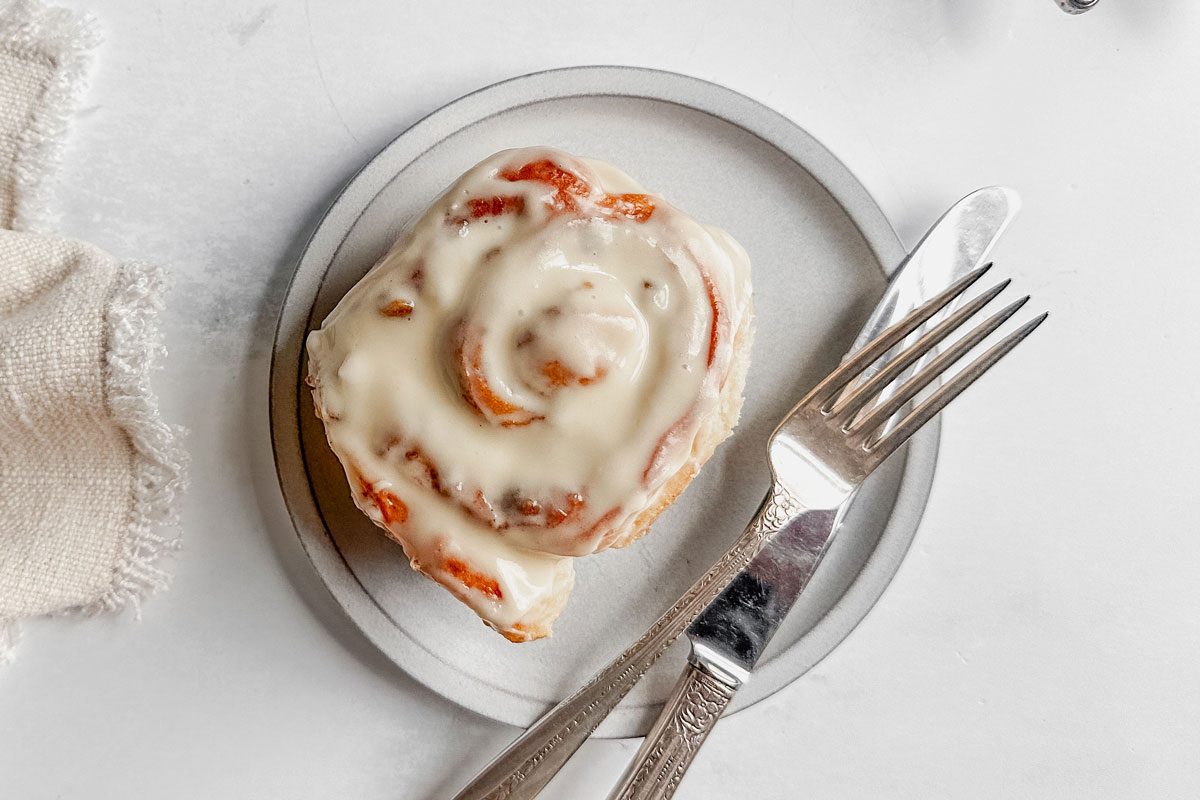 Taste of Home apple cinnamon roll on a white plate next to a cloth napkin on a marble surface.