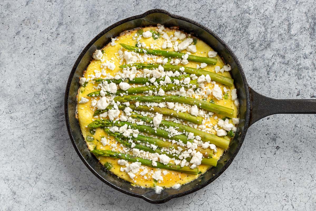 Taste of Home Asparagus Frittata recipe photo of the eggs in a skillet with garlic, green onions, chopped asparagus and topped with asparagus spears.
