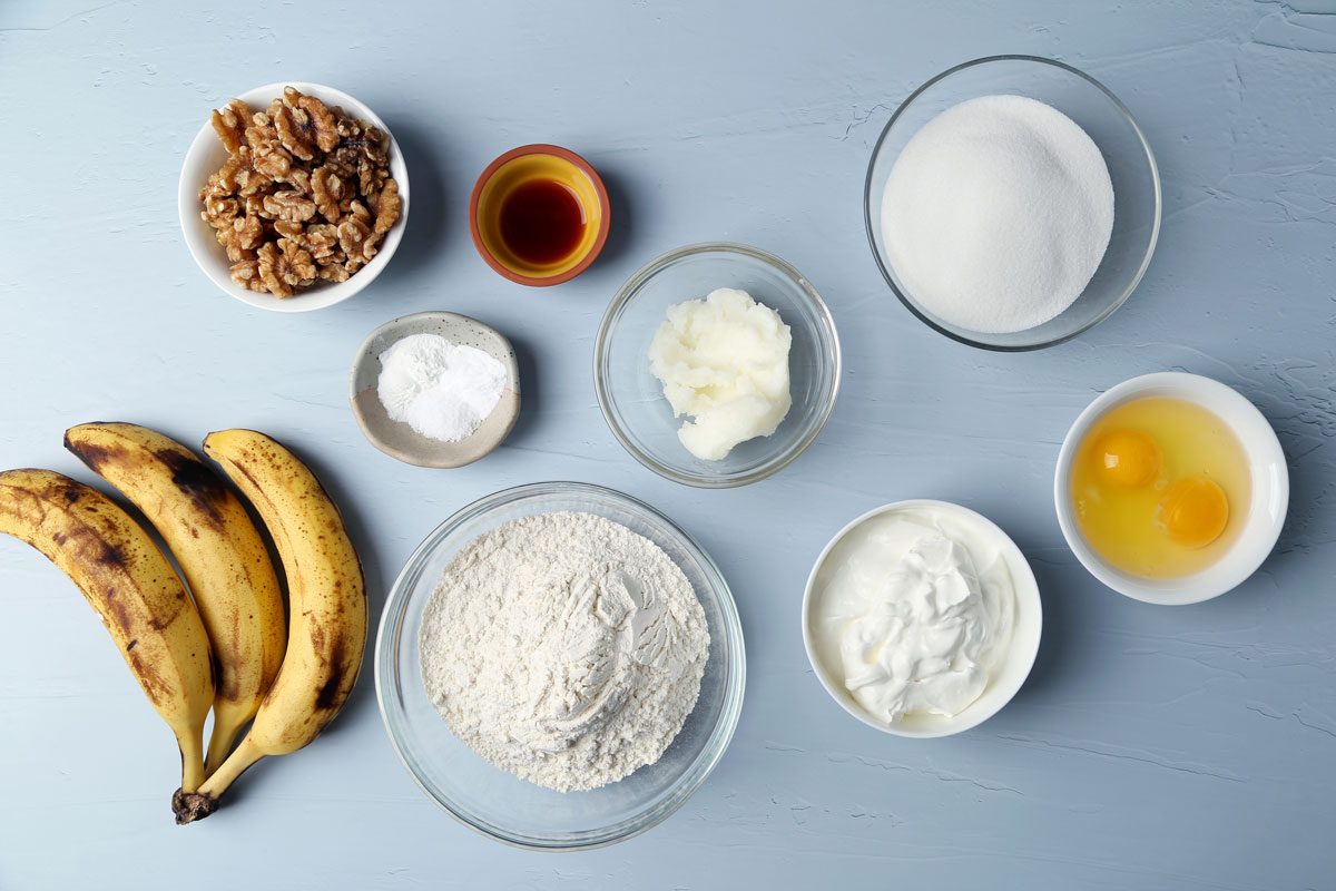 Ingredients laid out in various bowls for Taste of Home's Banana Bundt Cake on a blue surface.