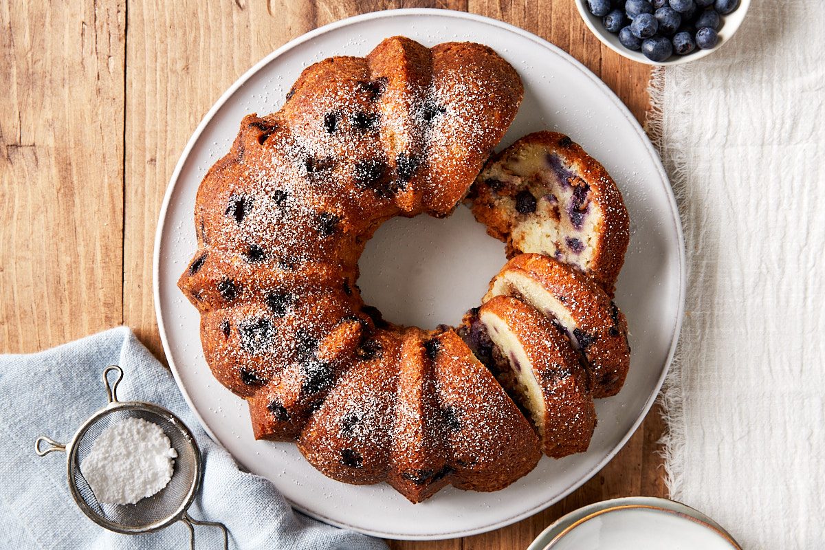 Blueberry Coffee Cake Hero Image, Cake on serving dish, partially sliced and dusted with powdered sugar