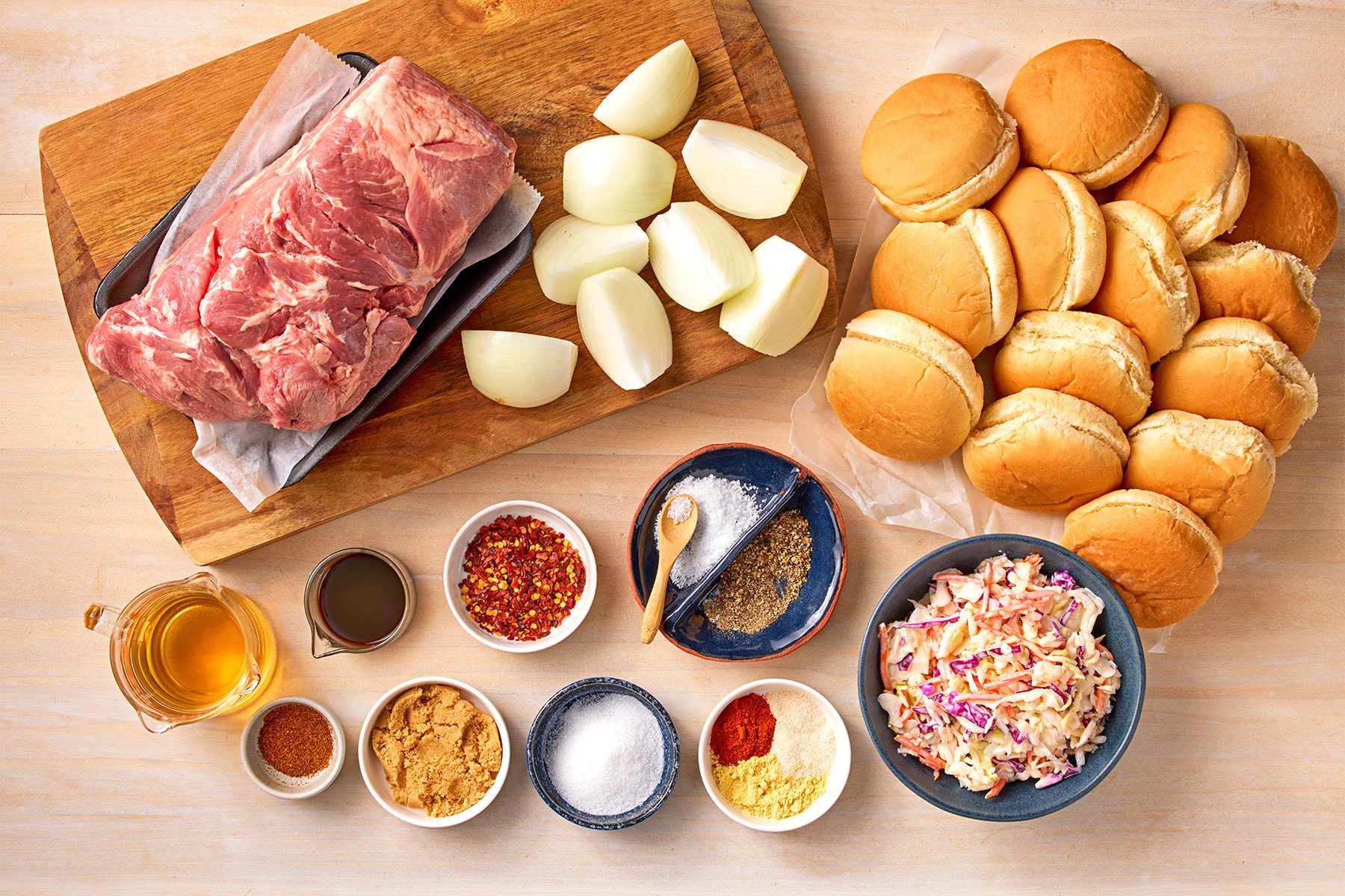 overhead shot; white textured background; Carolina-Style Pork Barbecue served over a tray with salad in small bowl, a small white over kitchen napkin; adding pork mixture over bun;