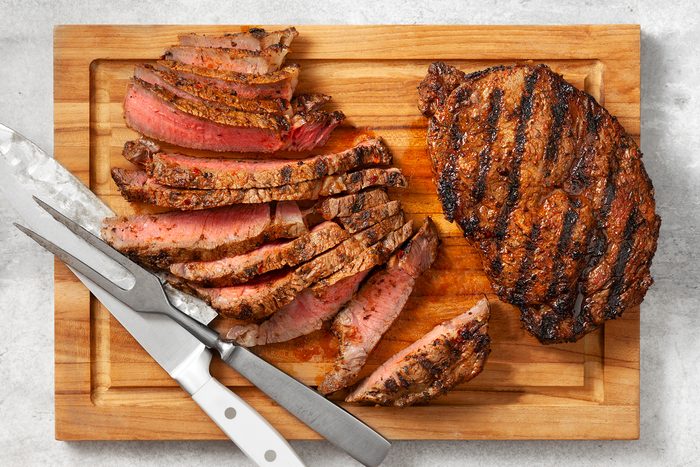 A wooden cutting board with a grilled steak, partially sliced. The steak has visible grill marks and is medium-rare in the center.