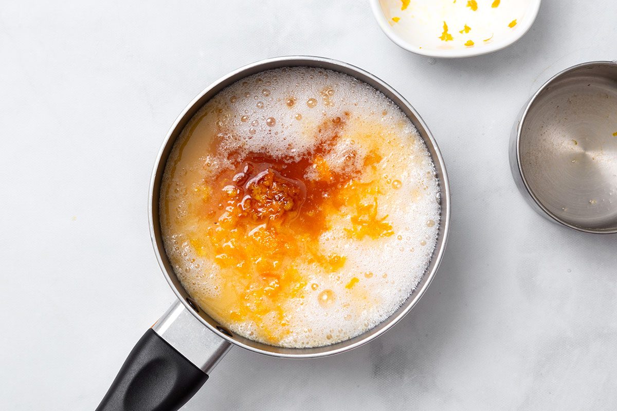 Heated milk in small saucepan with mixture of orange juice, orange zest, and vanilla for Step 1 of Orange Ice Cream for Taste of Home