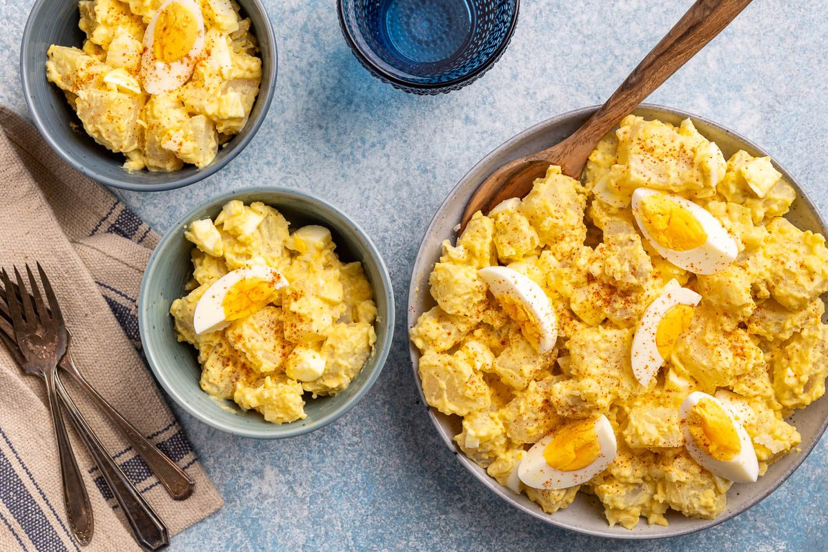 Taste of Home Potato Salad Recipe photo of the finished recipe dished out into bowls with forks, napkin and serving bowl.