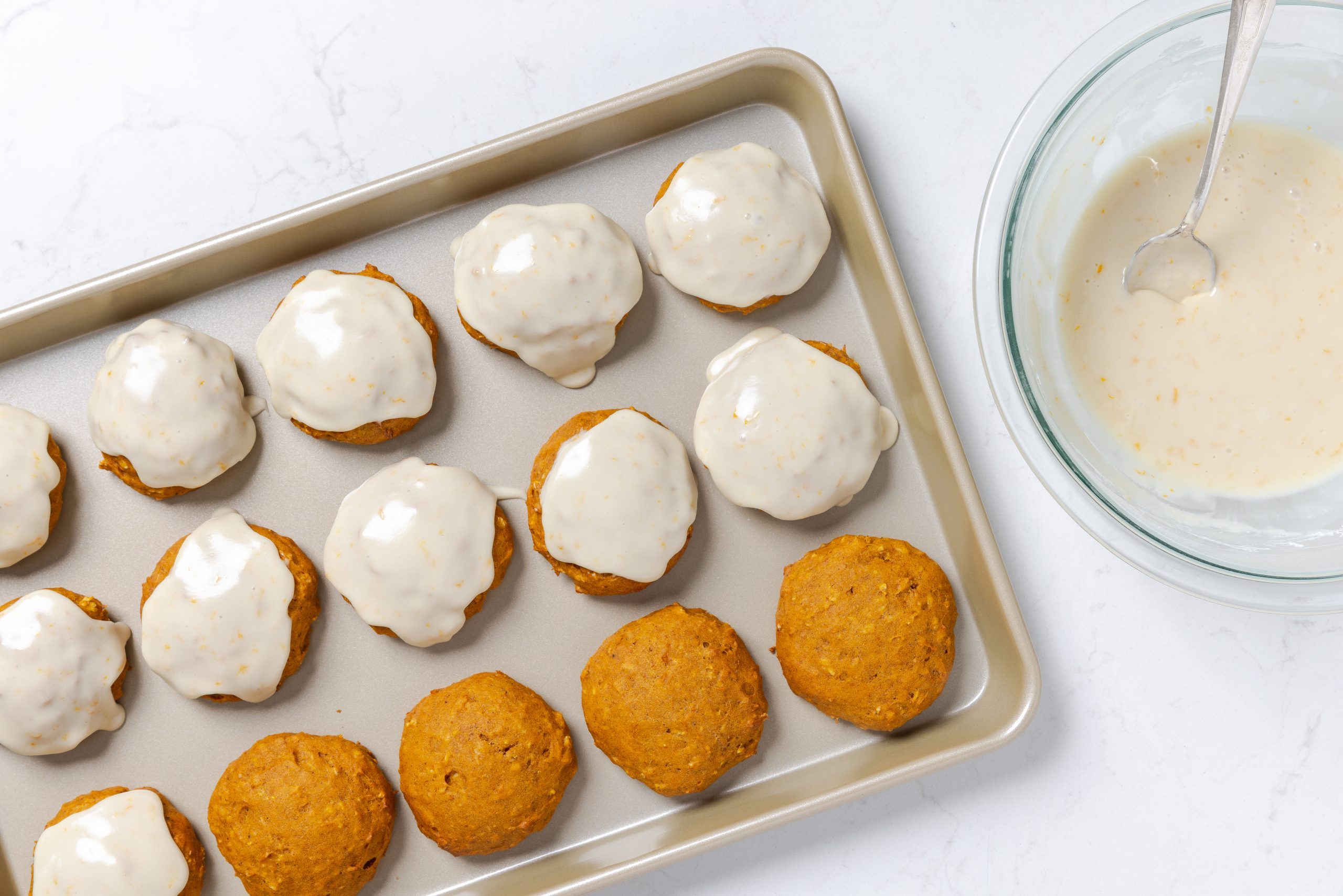 Cookies on baking sheet being frosted after baking.