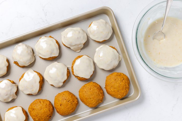 Cookies on baking sheet being frosted after baking.