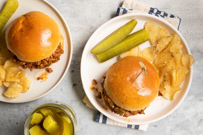 Top view of slow Cooker Sloppy Joes burgers served on two plates with potato chips and pickle