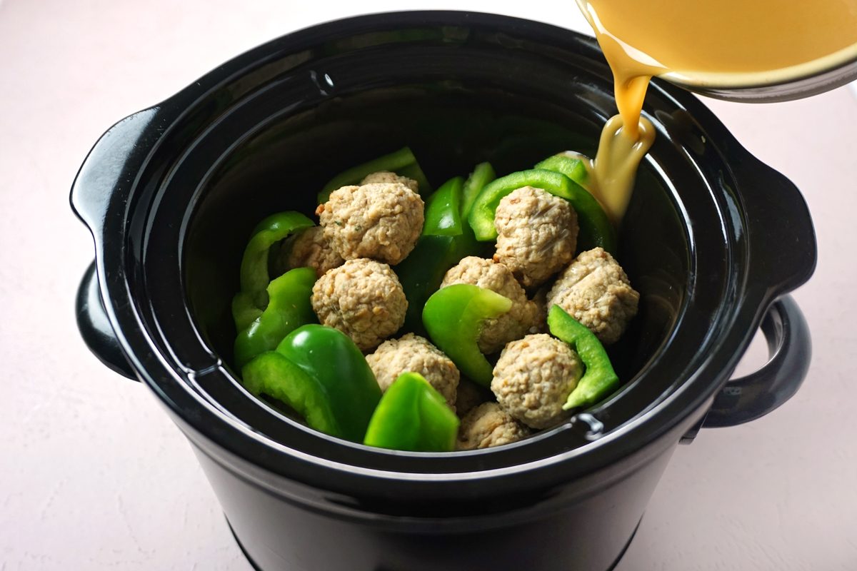 Pouring sauce over green peppers and meatballs in a crock pot to make slow cooker sweet and sour meatballs for Taste of Home RMS 27421