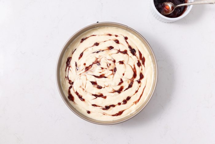 Cheesecake in springform pan with raspberry jam swirl.