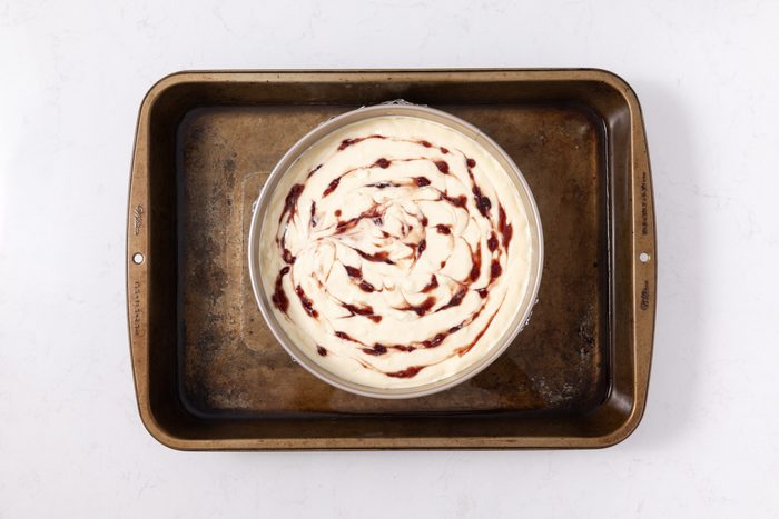 Cheesecake prepared to be baked in baking pan with water added to it.