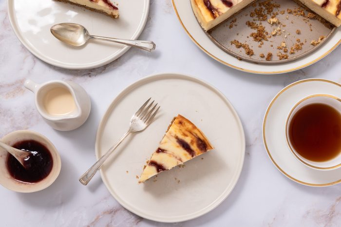Cheesecake slice served on plate with full cheesecake near it, served with tea, cream and jam.