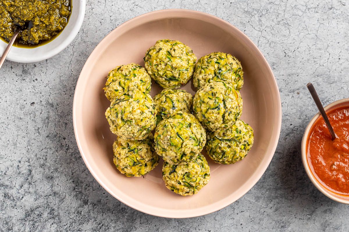 Taste of Home Zucchini Meatballs recipe photo of the finished recipe in a serving dish with pesto and marinara on the side.