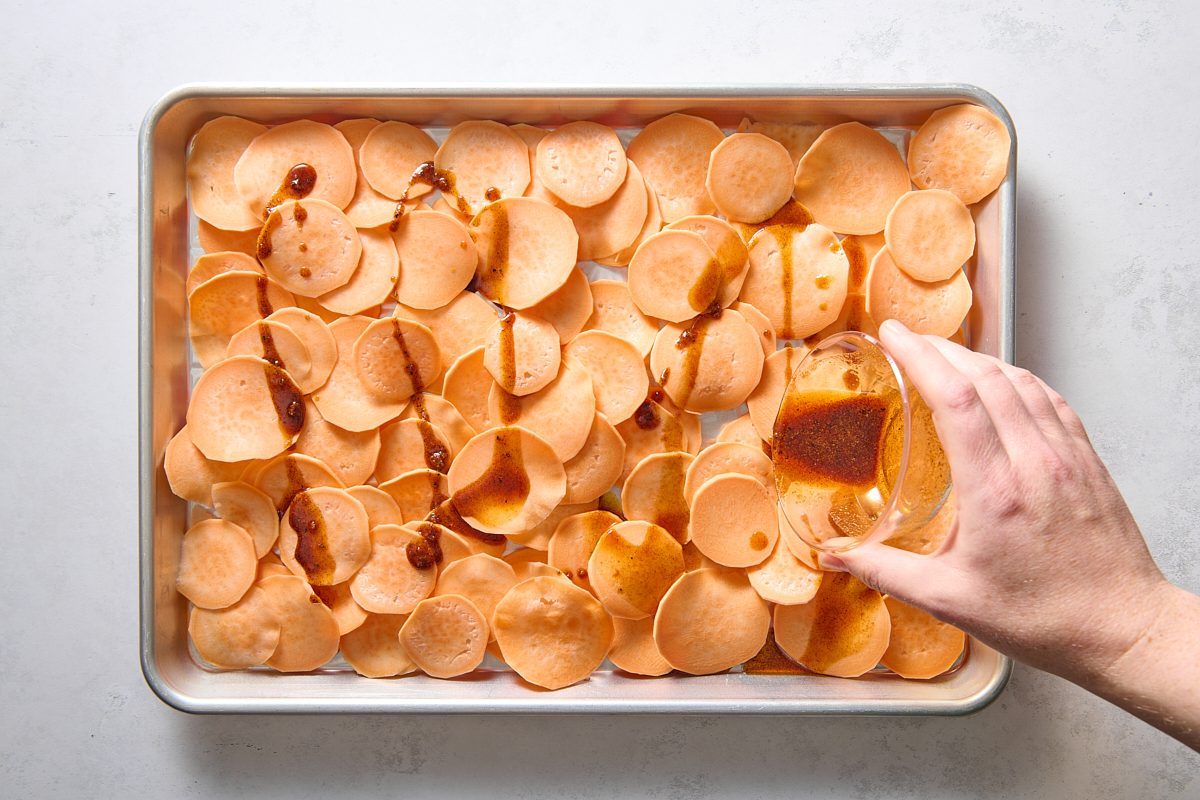 Pouring seasoned oil over the sweet potato slices