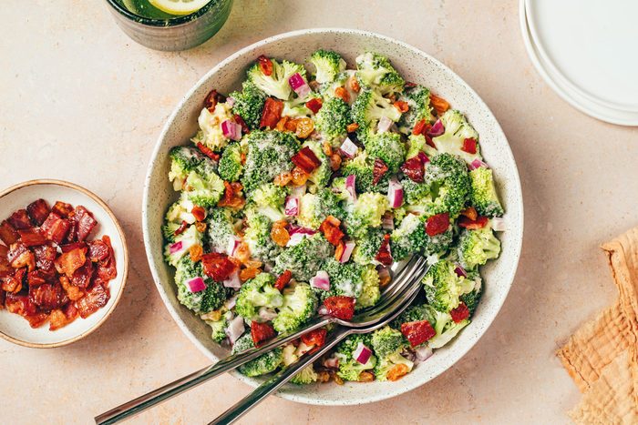 Broccoli Raisin Salad in a serving bowl with serving spoon and fork, topped with cooked ham, recipe for Taste of Home