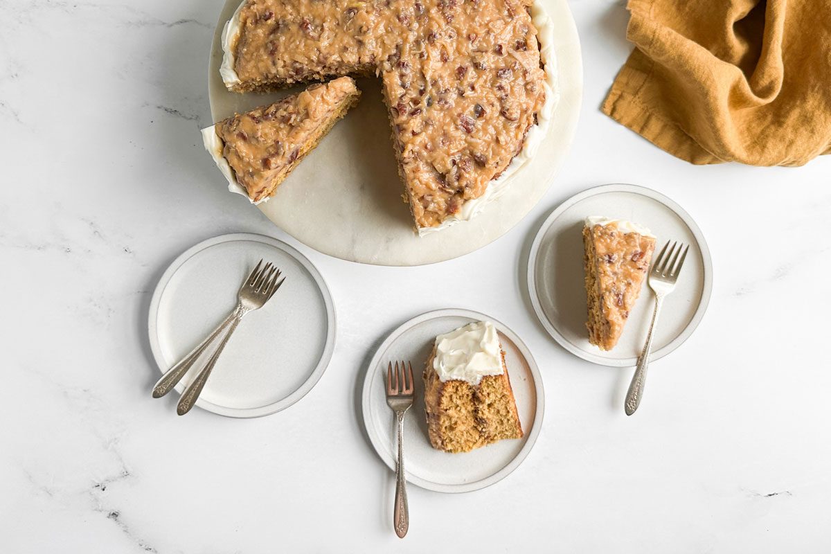Taste of Home Butterscotch Cake on a marble and wood cake stand with slices of cake on white plates