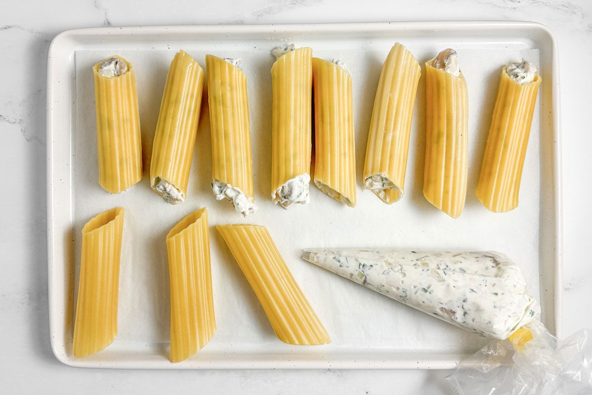 Filled and unfilled pasta for Taste of Home Chicken Manicotti on a white baking sheet