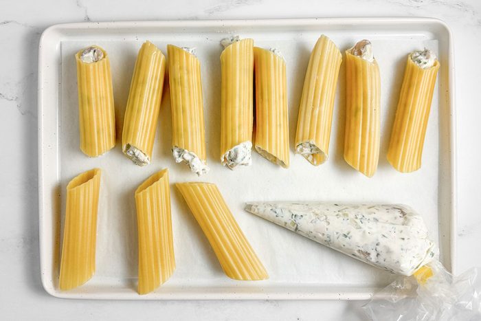 Filled and unfilled pasta for Taste of Home Chicken Manicotti on a white baking sheet