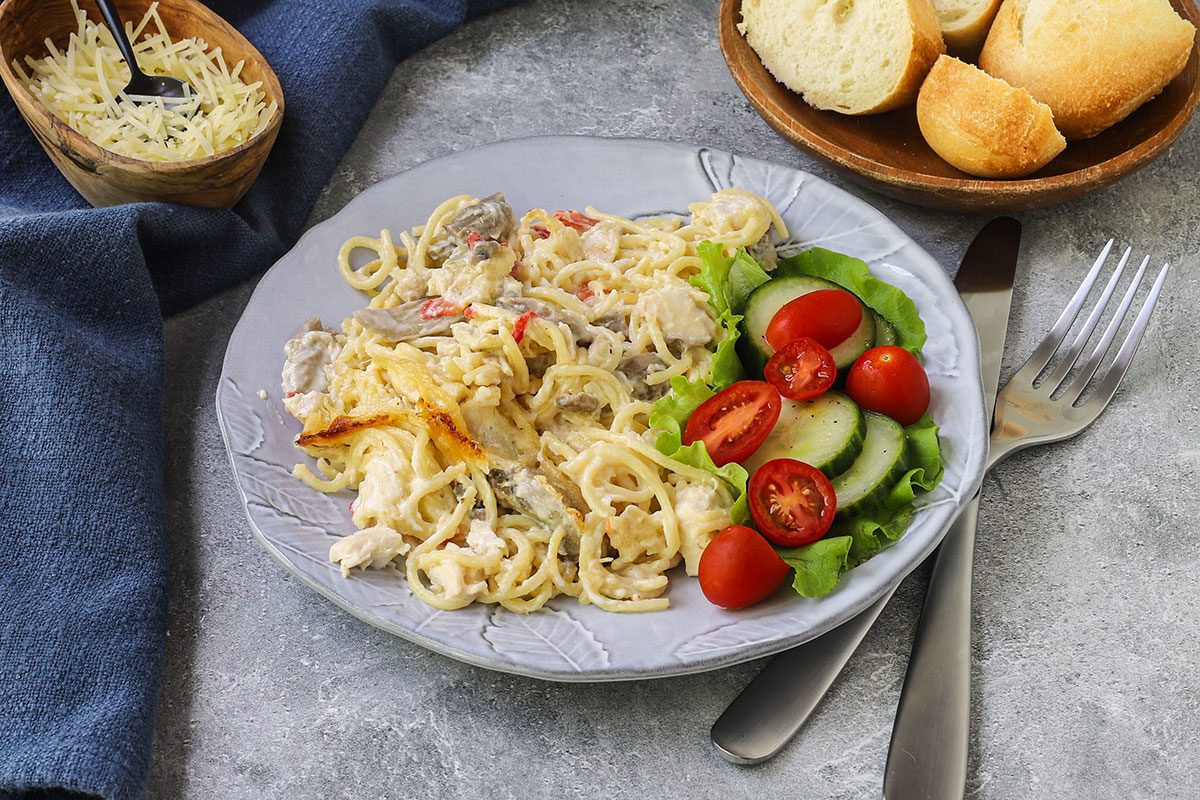 A serving of chicken tetrazzini with a small salad alongside and sliced baguette.