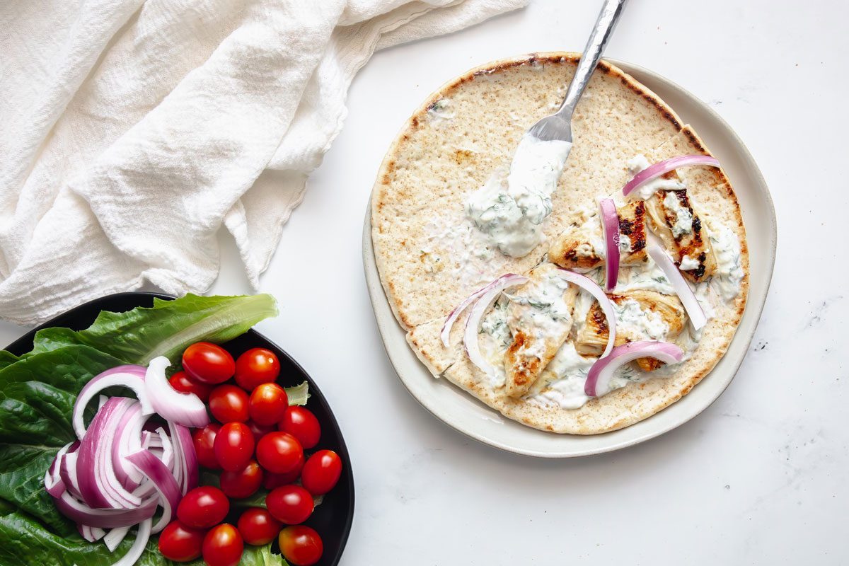 Overhead shot for Taste of Home Chicken Gyros assembled on a plate with additional toppings on a marble surface.