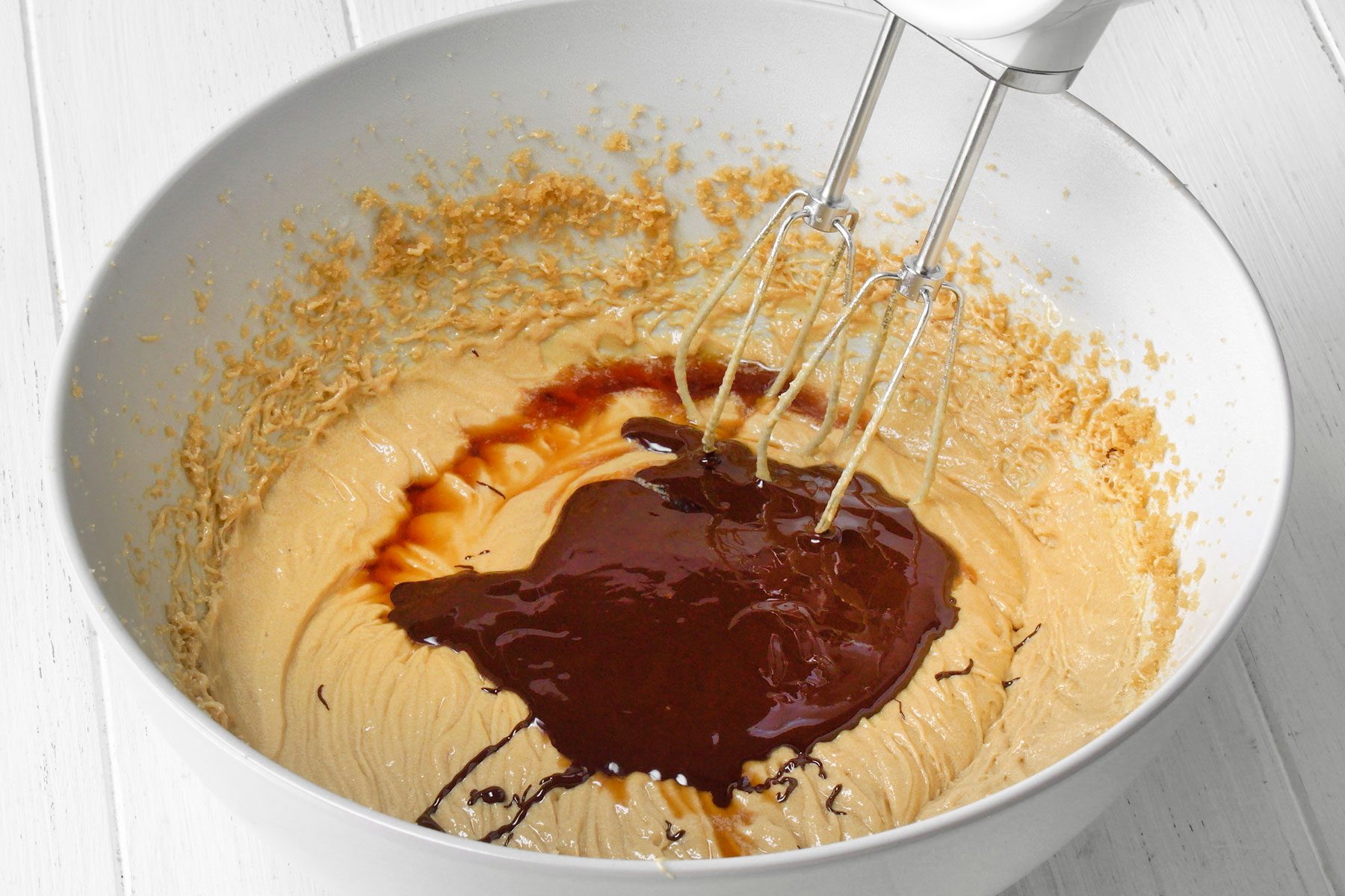 Vanilla extract and melted chocolate being added to butter, eggs and brown sugar mixture.