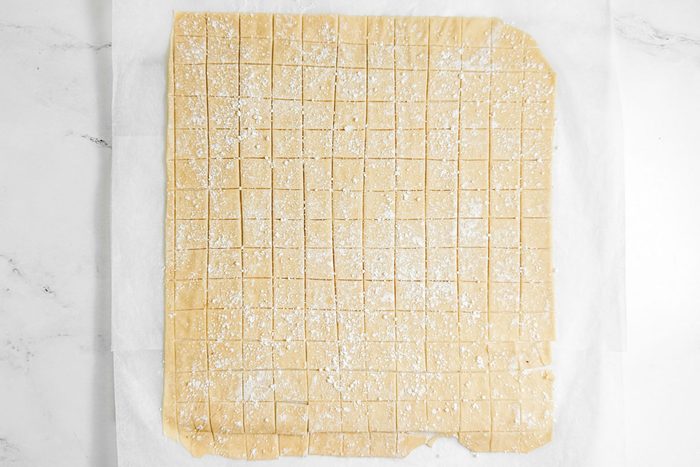 Dough squares for Taste of Home Copycat Cracker Barrel Chicken and Dumplings on parchment paper on a marble surface