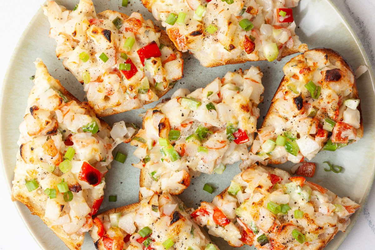 Full yield of Taste of Home Crab Salad Sandwiches on a green pate, garnished with green onions