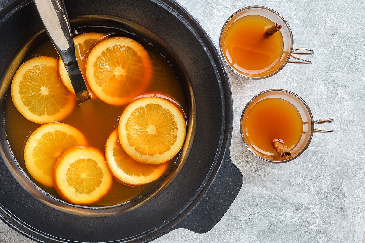 Spiced crockpot apple cider with ladle and filled cups on the side.