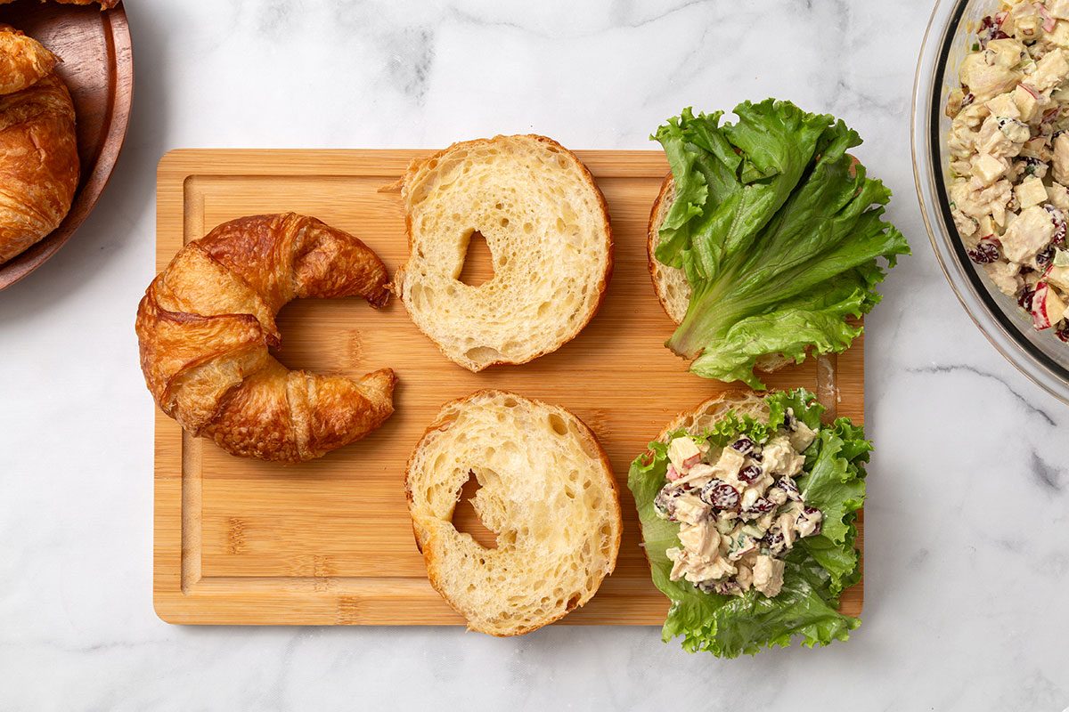 Sliced croissants with lettuce leaves and chicken salad layered on top of a cutting board 