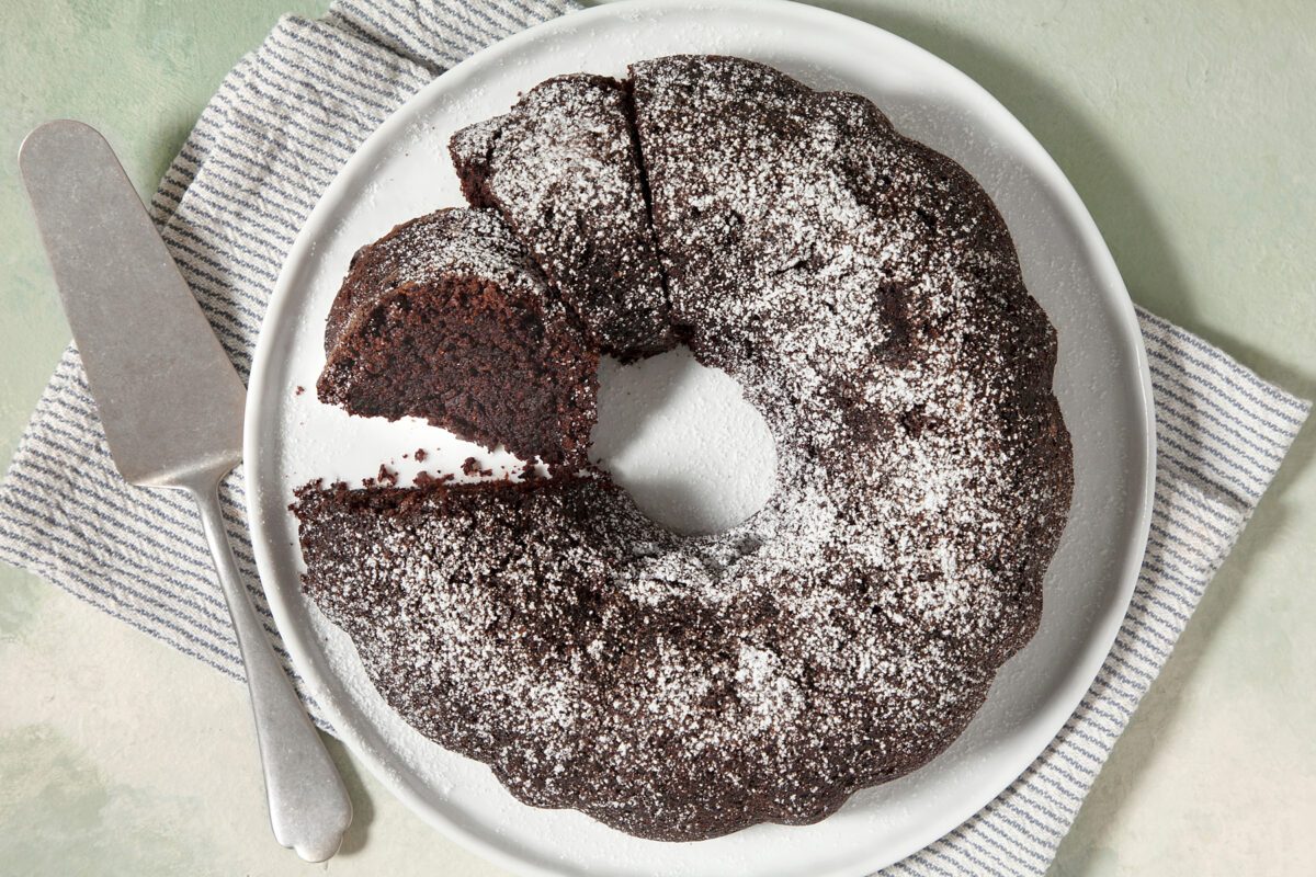overhead shot; light green textured background; A chocolate cake is displayed on a white plate; It