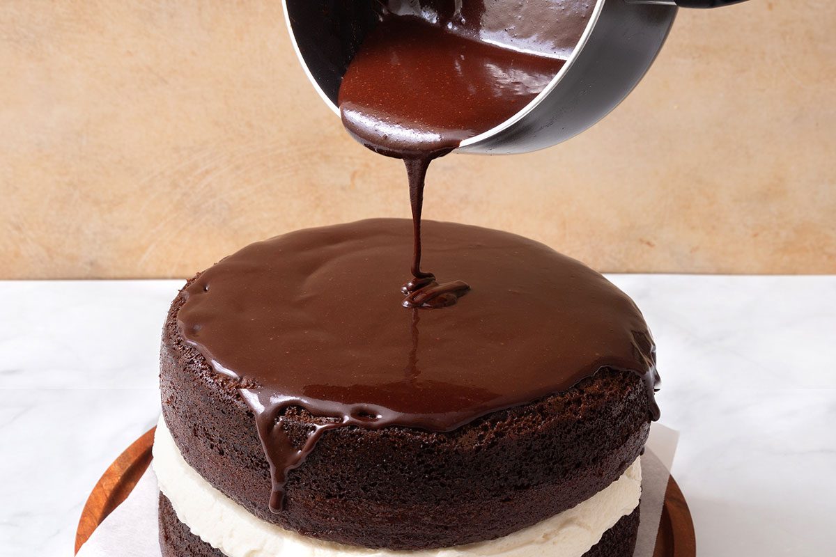 Chocolate glaze in a saucepan being poured over top of Ho Ho Cake for step three for Taste of Home