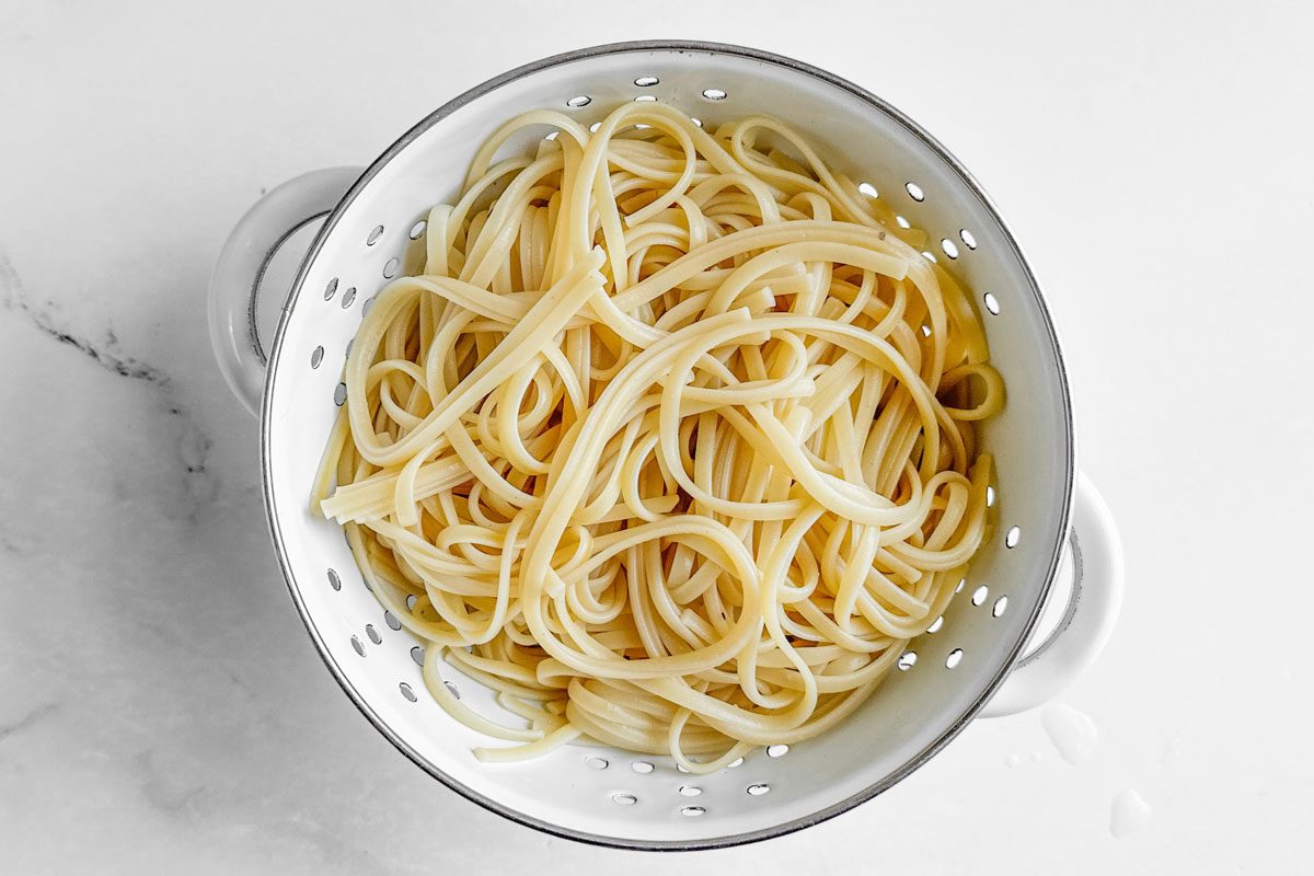 Drained linguine for Taste of Home Linguine with Clam Sauce in a white colandar on a marble surface