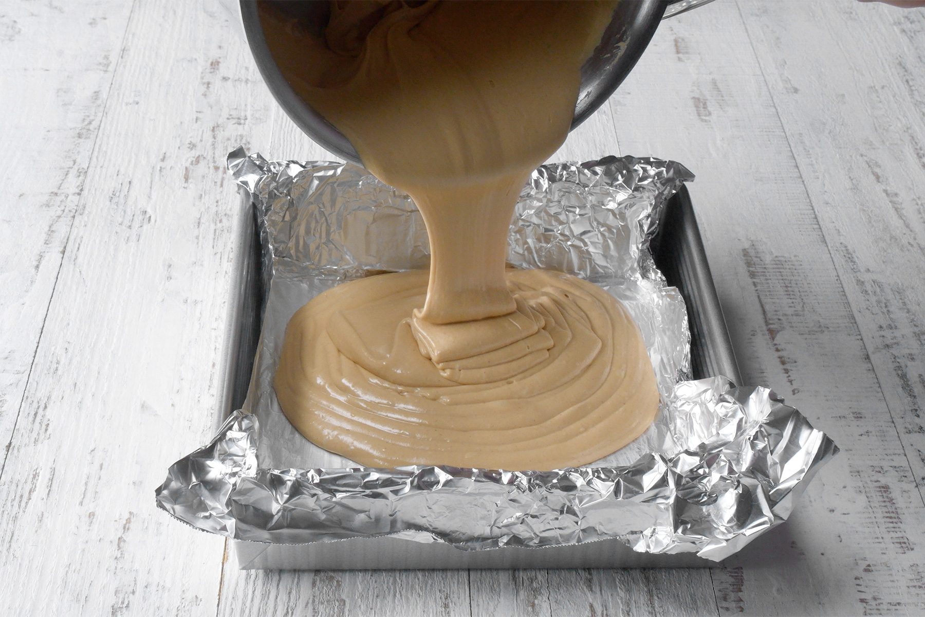 Angle view shot of pan with foil; immediately spread into prepared pan; white wooden background;