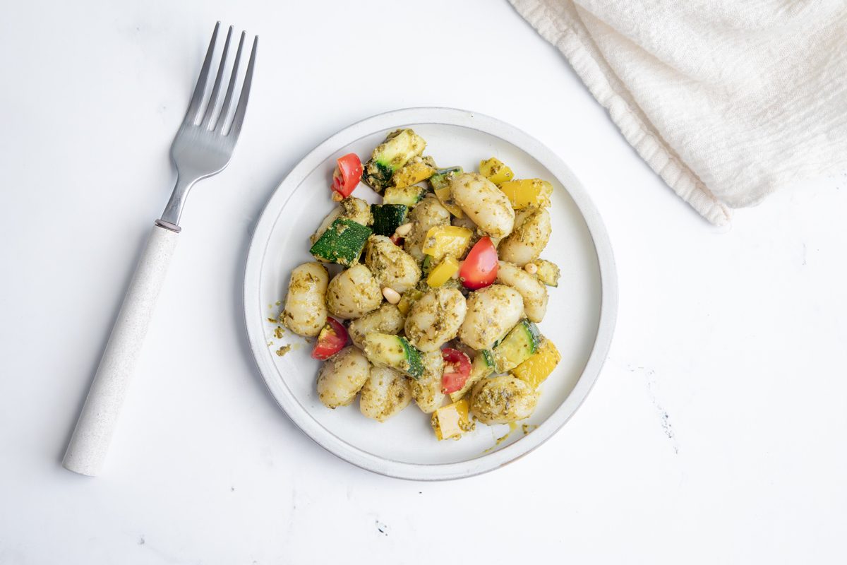 Overhead Beauty Shot for Taste of Home Pesto Gnocchi with one serving on a white plate on a marble surface.