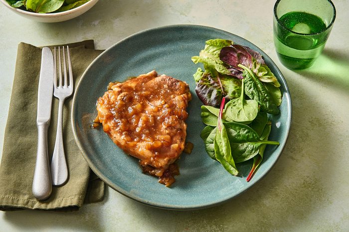 Angled shot of a portion of pork chops and applesauce on a plate with a green salad