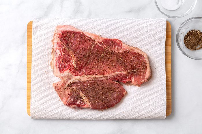 Porterhouse steak with salt and pepper on paper towels for step one of Porterhouse Steak recipe for Taste of Home