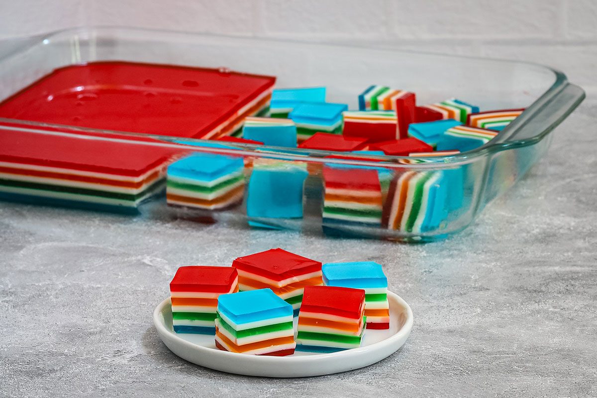Rainbow jello cubes on a plate with more in the background.