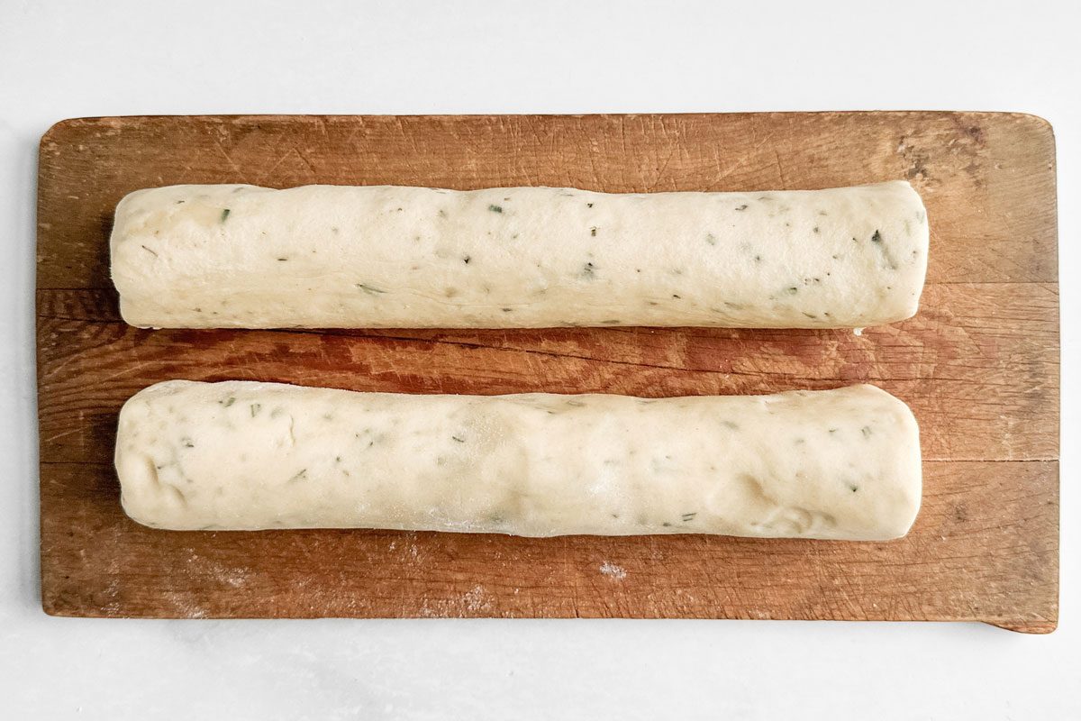 Unbaked logs for Taste of Home Rosemary Shortbread Cookies on a wooden board