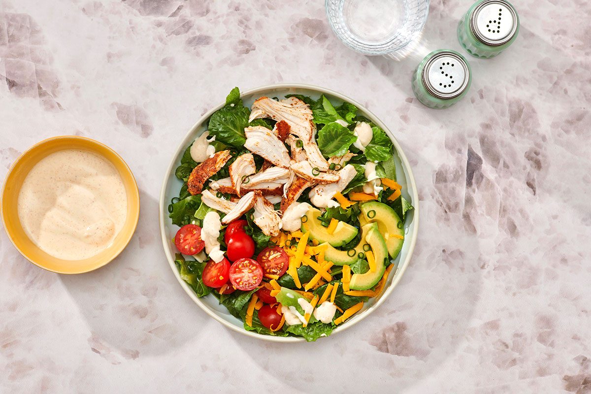 Chicken taco salad assembled on a serving plate with extra salad dressing on the side